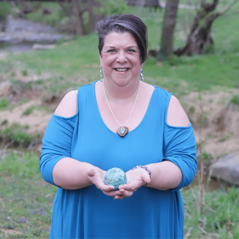 An Image of Yvette LeFlore from Healing with Yvette holding crystals with a blue top and nature as a background.